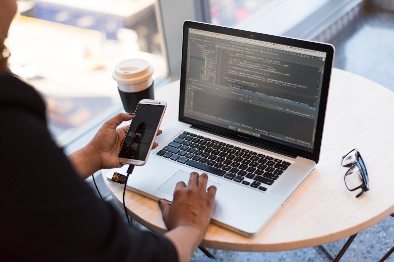 Mastering the First Impression: Your intriguing post title goes here Developer working remotely, coding on a laptop with phone in hand, showcasing modern work culture.
